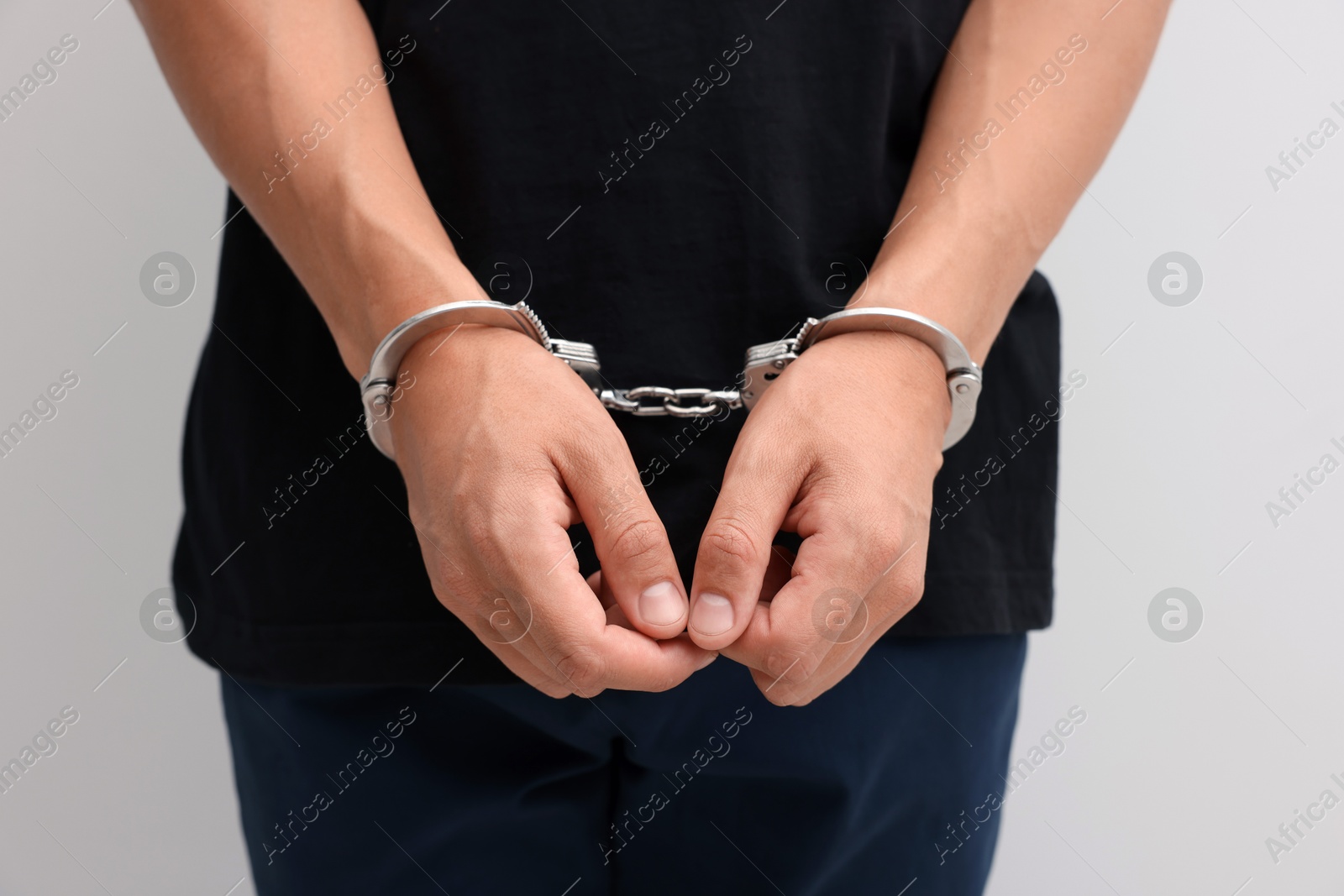 Photo of Man in metal handcuffs on light background, closeup