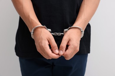 Photo of Man in metal handcuffs on light background, closeup