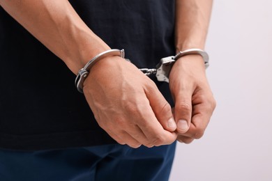 Photo of Man in metal handcuffs on light background, closeup