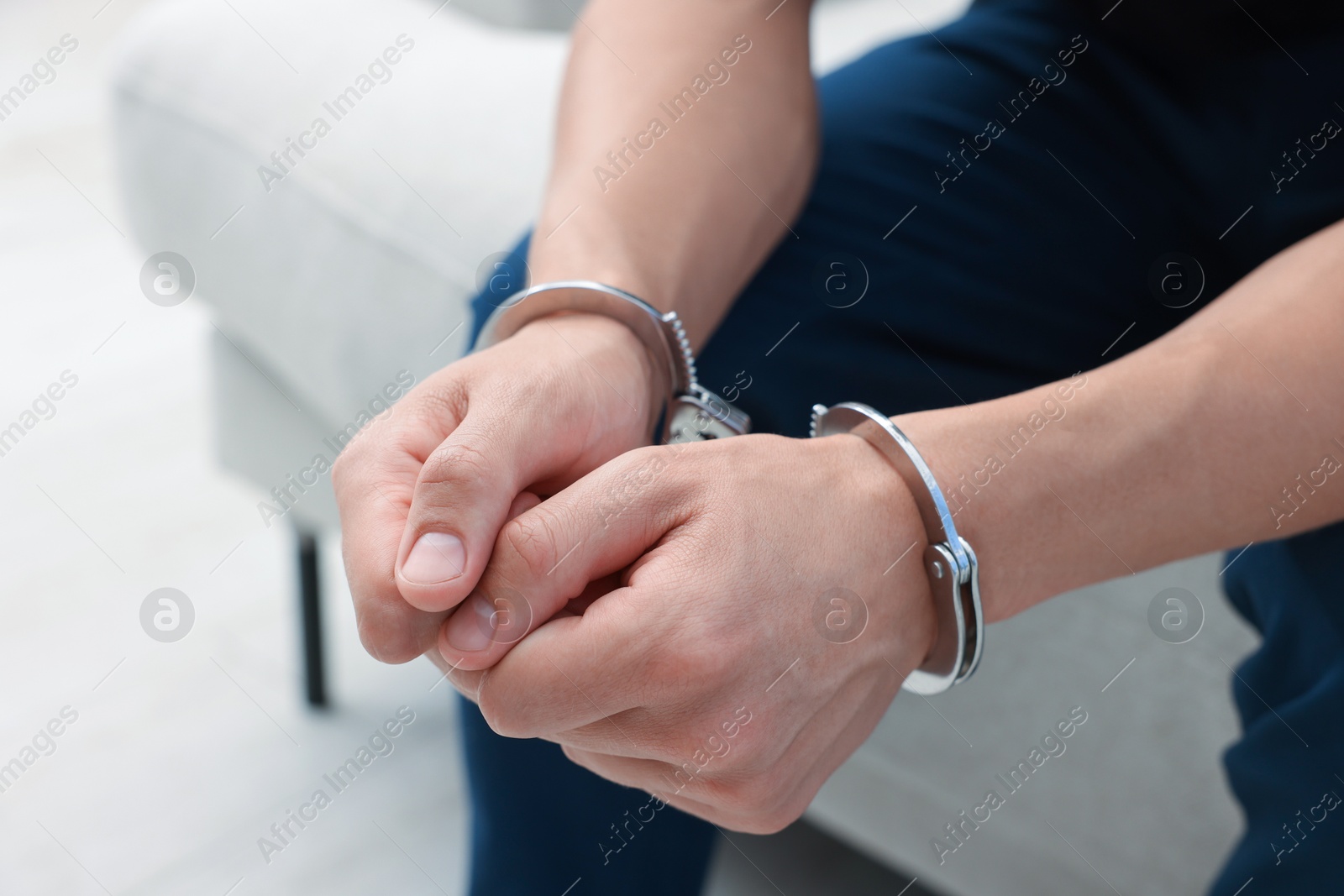 Photo of Man in metal handcuffs sitting on sofa indoors, closeup