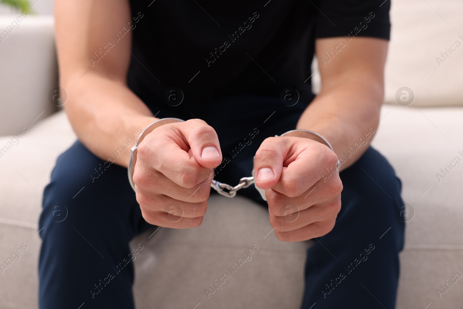 Man in metal handcuffs sitting on sofa indoors, closeup Photo of Man in metal handcuffs sitting on sofa indoors, closeup