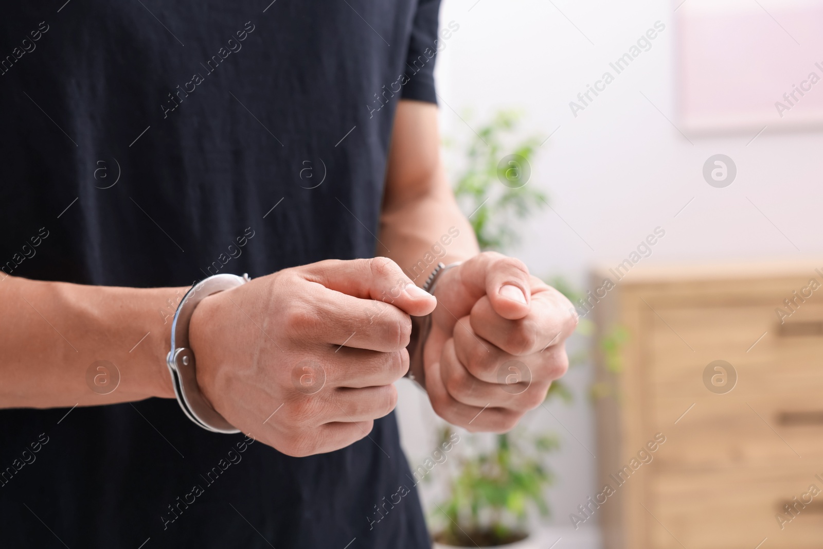 Photo of Man in metal handcuffs indoors, closeup. Space for text