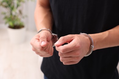 Photo of Man in metal handcuffs indoors, closeup view