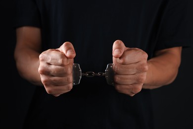 Photo of Man in metal handcuffs on black background, closeup