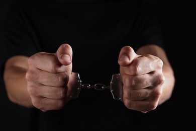 Photo of Man in metal handcuffs on black background, closeup