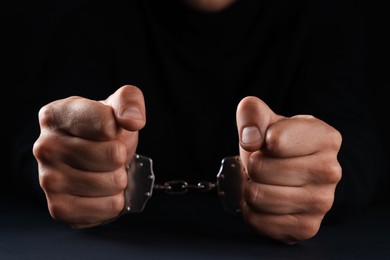 Photo of Man in metal handcuffs on black background, closeup