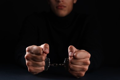 Photo of Man in metal handcuffs on black background, closeup