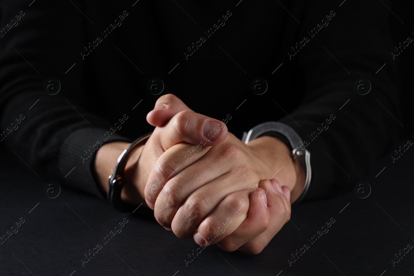 Photo of Man in metal handcuffs on black background, closeup
