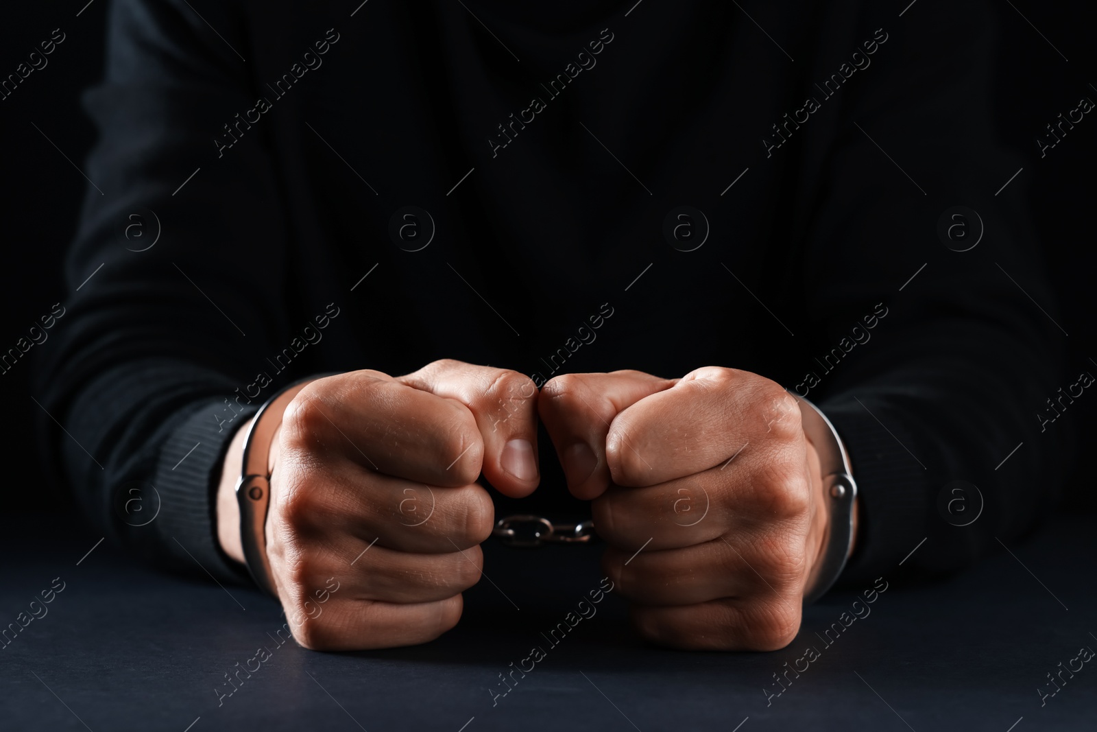 Man in metal handcuffs at table on black background, closeup Photo of Man in metal handcuffs at table on black background, closeup