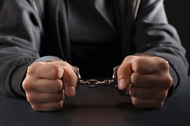 Photo of Woman in metal handcuffs at table on black background, closeup