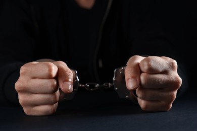 Photo of Woman in metal handcuffs at table on black background, closeup