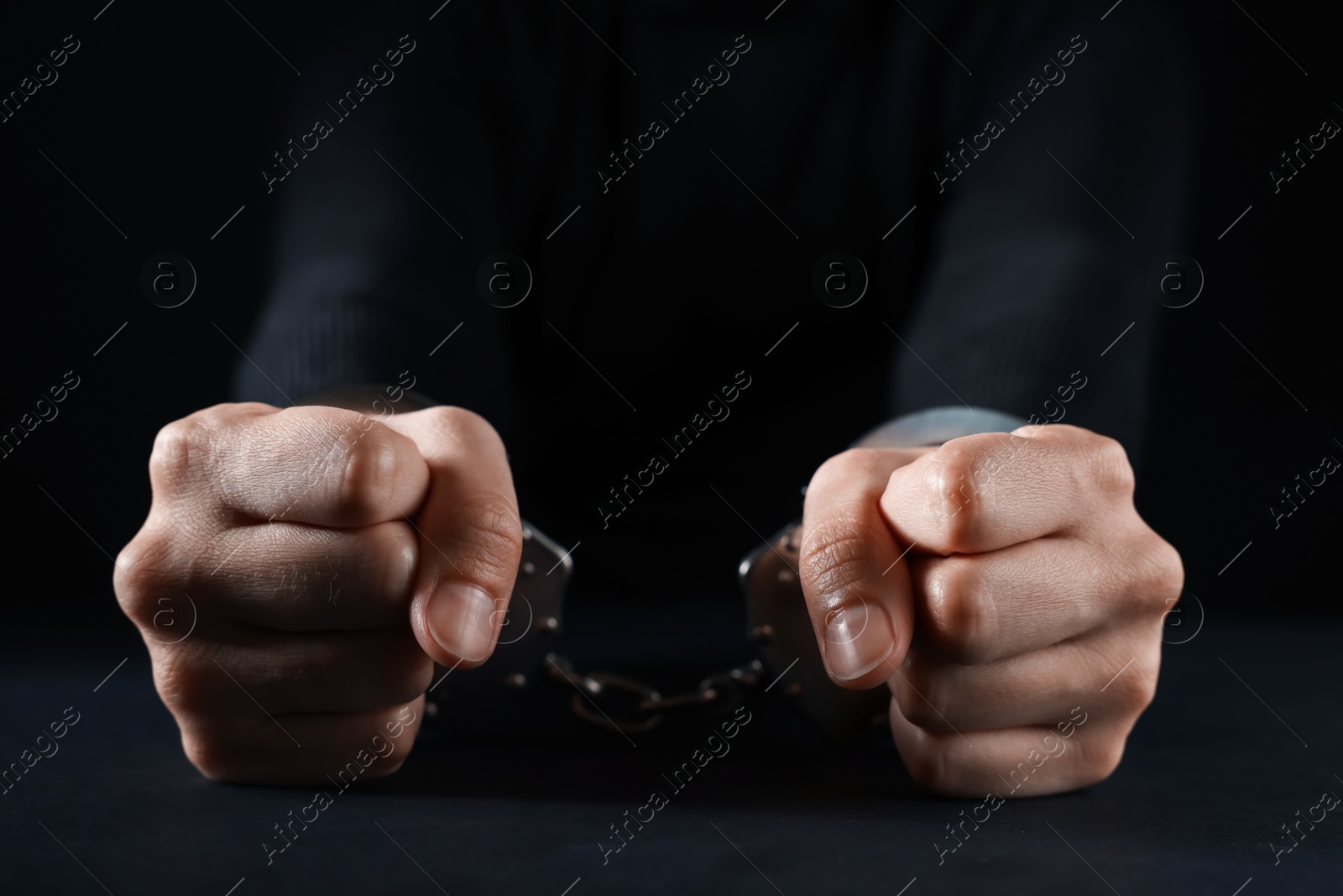 Photo of Woman in metal handcuffs at table on black background, closeup