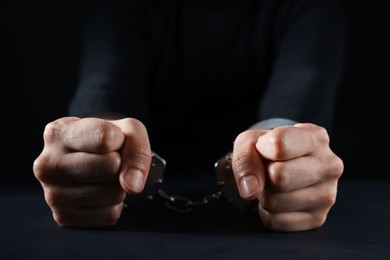 Photo of Woman in metal handcuffs at table on black background, closeup