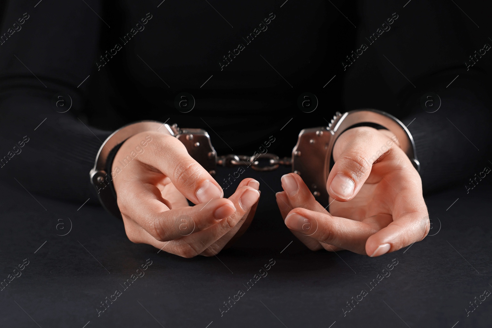 Photo of Woman in metal handcuffs at table on black background, closeup