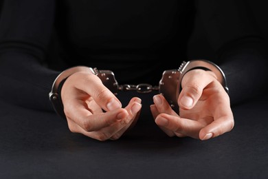 Photo of Woman in metal handcuffs at table on black background, closeup
