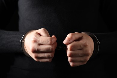 Photo of Woman in metal handcuffs on black background, closeup