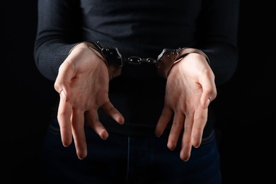 Photo of Woman in metal handcuffs on black background, closeup