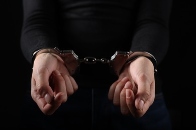Photo of Woman in metal handcuffs on black background, closeup