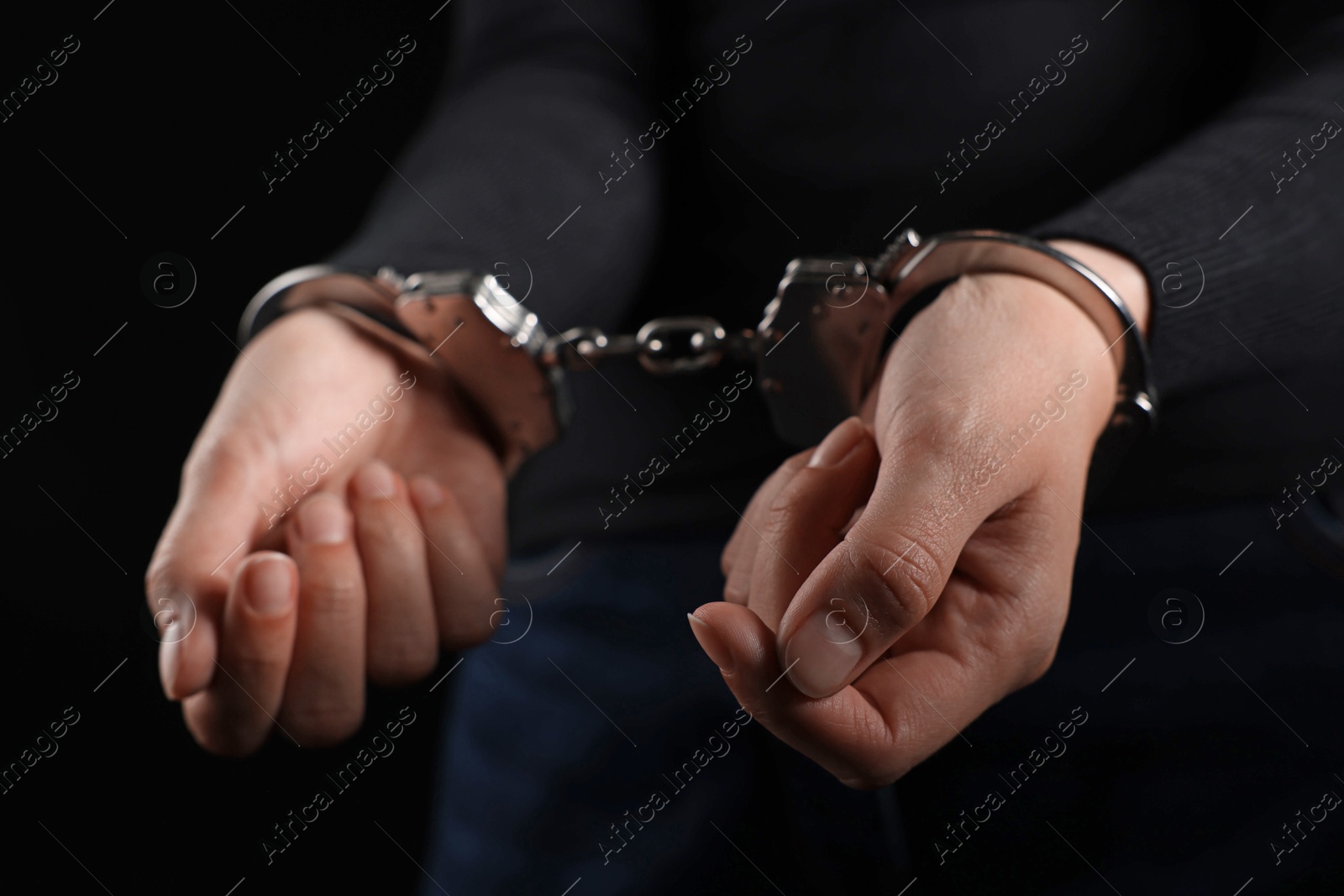 Photo of Woman in metal handcuffs on black background, closeup