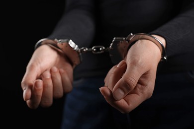 Photo of Woman in metal handcuffs on black background, closeup