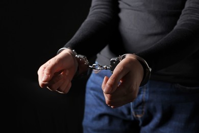 Photo of Woman in metal handcuffs on black background, closeup
