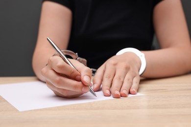 Photo of Woman in metal handcuffs writing something at wooden table against grey background, closeup