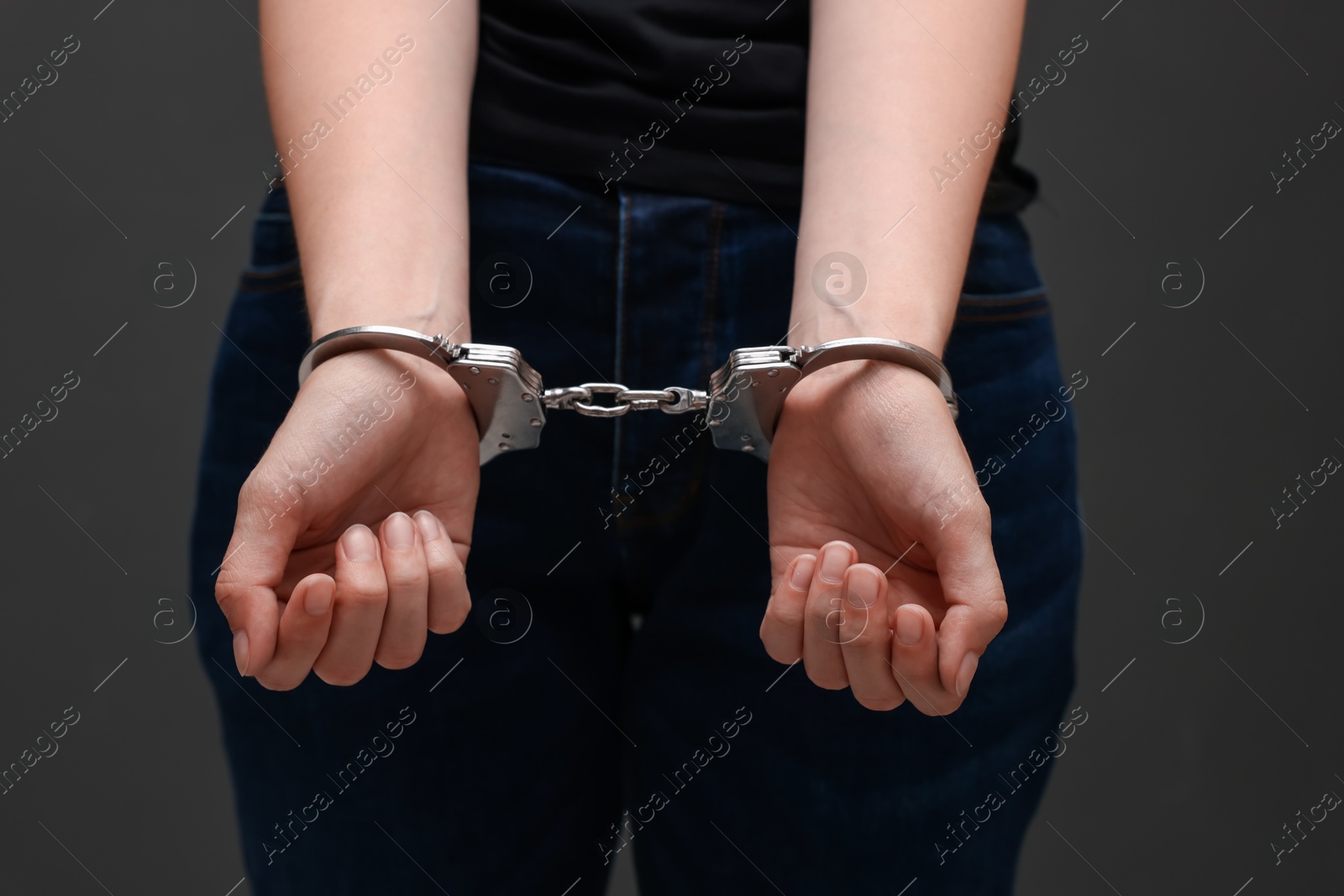 Photo of Woman in metal handcuffs near grey wall, closeup
