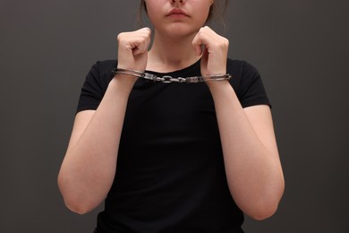 Photo of Woman in metal handcuffs near grey wall, closeup