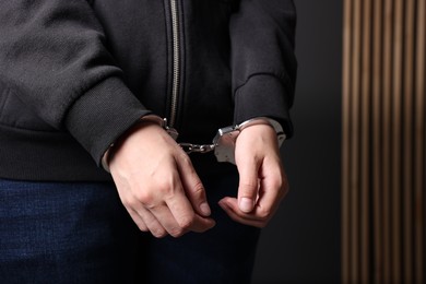 Photo of Woman in metal handcuffs near grey wall, closeup