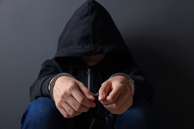 Photo of Woman in metal handcuffs and hoodie near grey wall