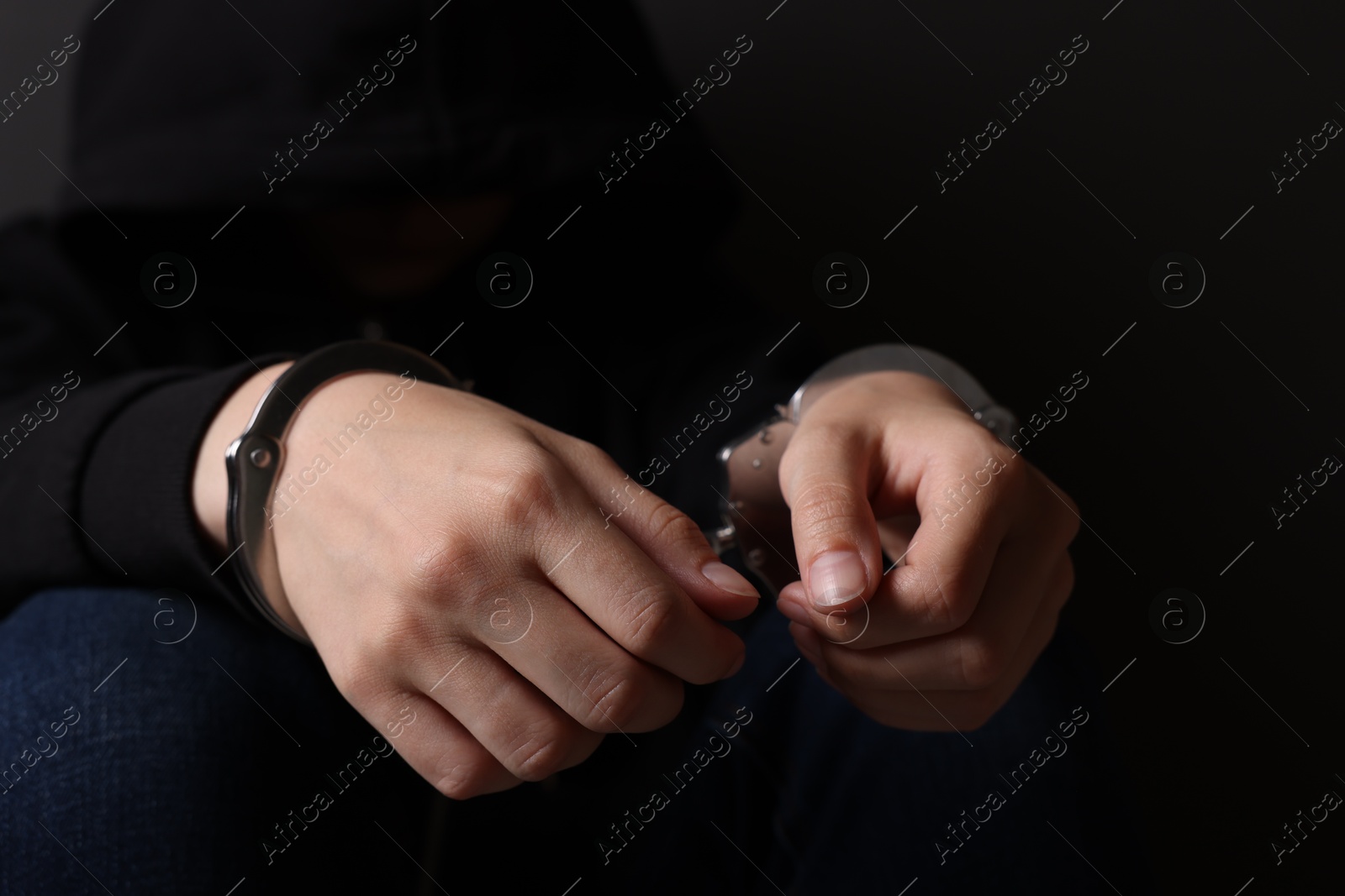 Photo of Woman in metal handcuffs on dark background, closeup