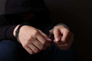 Photo of Woman in metal handcuffs on dark background, closeup