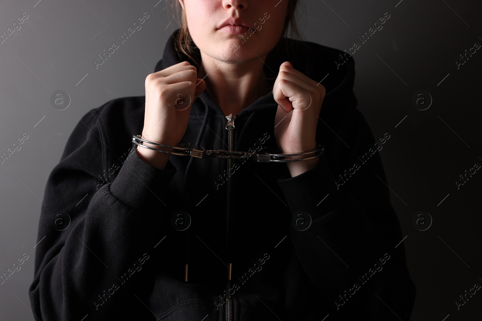 Photo of Woman in metal handcuffs near grey wall, closeup