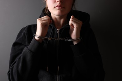 Photo of Woman in metal handcuffs near grey wall, closeup