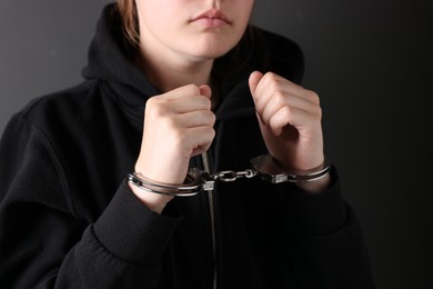 Photo of Woman in metal handcuffs near grey wall, closeup