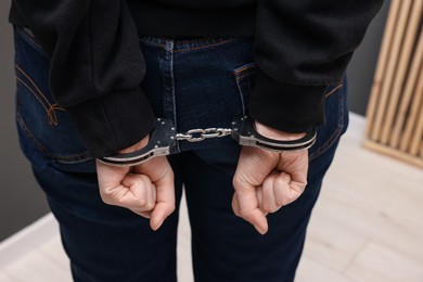 Photo of Woman in metal handcuffs indoors, back view