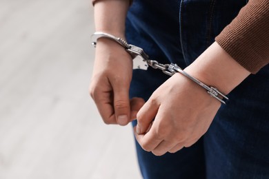 Photo of Woman in metal handcuffs on blurred light background, closeup. Space for text