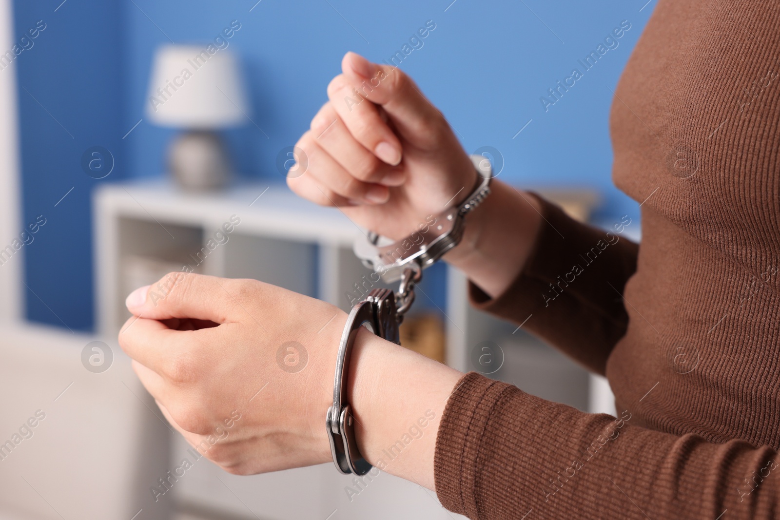 Photo of Woman in metal handcuffs indoors, closeup view