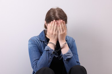 Photo of Woman in metal handcuffs covering face with hands near light grey wall