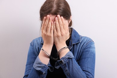 Photo of Woman in metal handcuffs covering face with hands near light grey wall