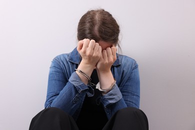 Photo of Woman in metal handcuffs covering face with hands near light grey wall