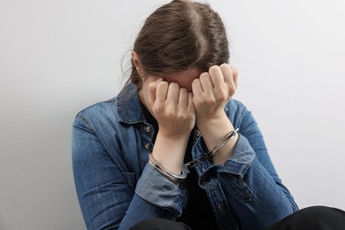 Photo of Woman in metal handcuffs covering face with hands near light grey wall