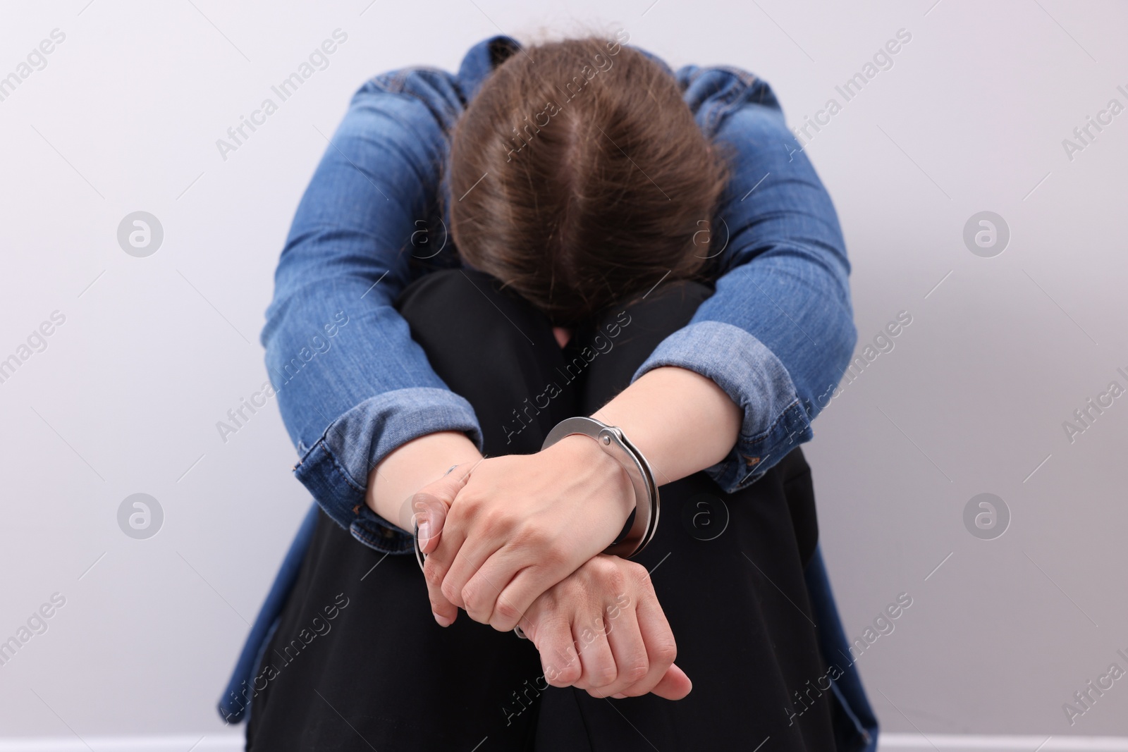 Photo of Woman in metal handcuffs near light grey wall