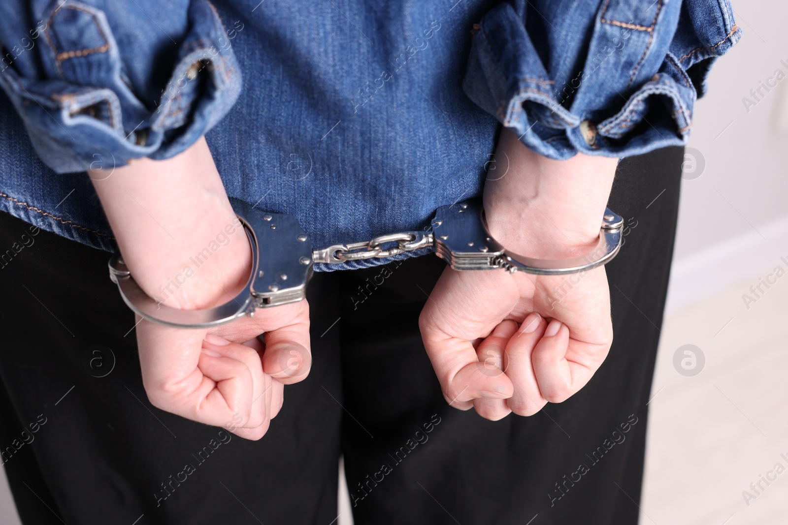 Photo of Woman in metal handcuffs indoors, back view