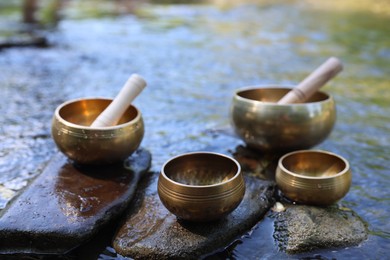 Photo of Tibetan singing bowls with mallets on stones in river, closeup