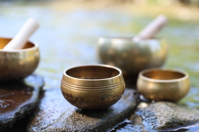 Photo of Tibetan singing bowls with mallets on stones in river, closeup