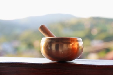 Photo of Tibetan singing bowl with mallet on handrail outdoors, closeup