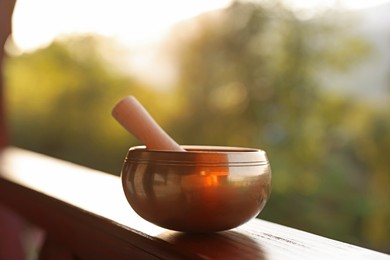 Photo of Tibetan singing bowl with mallet on handrail outdoors, closeup
