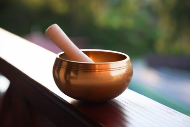 Photo of Tibetan singing bowl with mallet on handrail outdoors, closeup