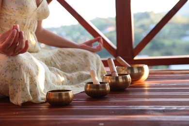 Photo of Woman practicing yoga near singing bowls on floor outdoors, closeup